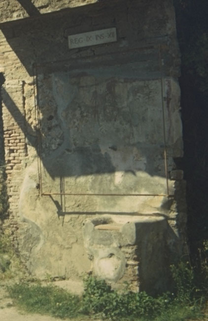 Street shrine outside IX.12.7. Detail from 1912 photograph. Bottom right painting: Fröhlich described two garlands with five persons in white garments in a semicircle, probably the vicomagistri and a tibicen. Jacobelli described them as five priests or magistri vici in the act of making a sacrifice. She also stated that this painting covered an older one on the same subject and perhaps it was meant to conceal the Genius of Augustus/Nero, affected posthumously by the damnatio memoriae, which dictated that the emperor’s name and image be wiped out wherever they appeared. See Fröhlich, T., 1991. Lararien und Fassadenbilder in den Vesuvstädten. Mainz: von Zabern. (p. 339, F71, T: 58,2). See Jacobelli, L., 2003. Gladiators at Pompeii. Rome: L’Erma di Bretschneider. (p. 85; Figs 69-70).