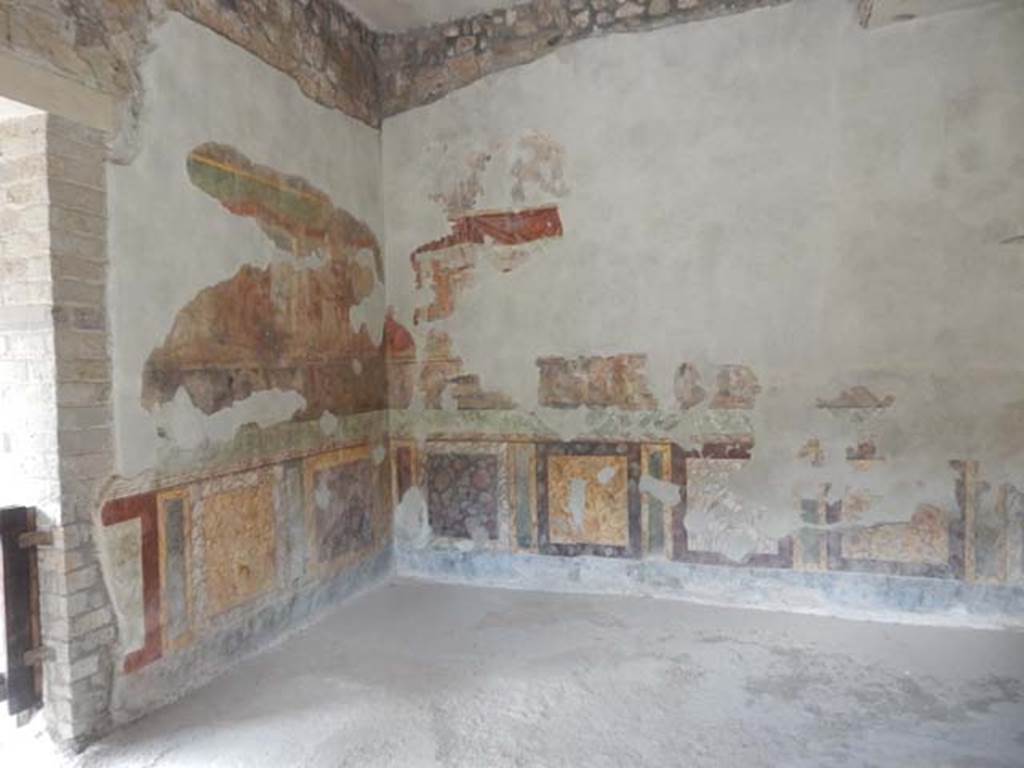 II.2.2 Pompeii. May 2016. Room “h”, looking towards the west wall and north-west corner.
Photo courtesy of Buzz Ferebee.
Della Corte identifies the following scenes in the narrow central frieze:

North wall: 
A group of heroes with the inscription ….YGES (possibly Phryges) [at extreme west end]
[Following] Patrocles fighting on a wagon and with the arms of Achilles, with the inscriptions XANTUS, BADIUS and PATROCLOS
[Following the previous] Thetis gives the weapons to her son; Automedon readies the chariot: with the inscriptions THETIS, BADIUS, ACHiLL[e]S and AUTO[me]DON
At the east extremity, after a gap whose fragments were perhaps dispersed in preceding explorations, the body of Hector dragged by the chariot. With the inscriptions [hect]OR and AUTOMEDON

East wall:
The Funeral of Patroclus
Games in his honour
Ransom of body of Hector

South wall: (Left to right)
Apollo firing arrows causing a plague throughout the Greek army [West end]
A horse is being watered, guarded by a hero [opposite end]

West wall:
Scene of combat with inscriptions to DANAUS and …AON
Scene of combat with inscriptions to AI(ax) TELAMONIUS and HECTOR

See Della Corte in Maiuri, A., 1928. Nuovi Scavi nella Via dell’Abbondanza. Milano: Hoepli. (p. 111-2).
