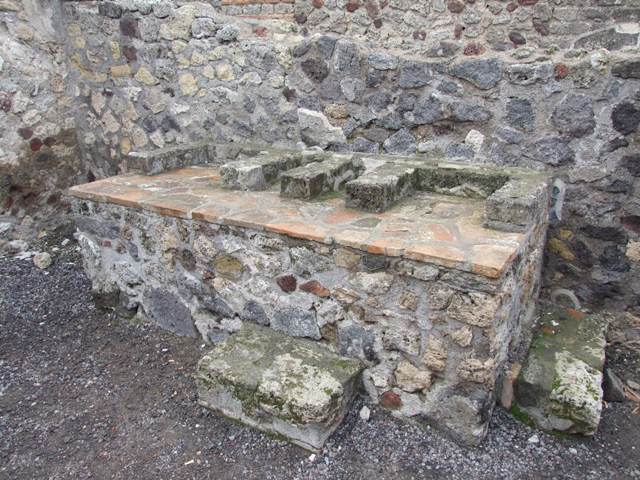 VI.6.1 Pompeii. Room 16, kitchen area in north-west corner of peristyle.
Sketch of the painted lararium that was found on the north wall, but no longer visible. A genius stood to the right of a blazing round altar. A very small tibicen was to the left of the altar. A tall wreathed Lar, dressed in blue tunic, red Pallium and high boots stood on each side.
Each Lar was pouring wine from a rhyton to a situla, Garlands and bushes were also in the scene. In the lower part two huge serpents, in a background of plants, confronted a round altar which had offerings.
See Boyce G. K., 1937. Corpus of the Lararia of Pompeii. Rome: MAAR 14. (p.46, no.156, Plate 18,1 ).
See Mazois, F., 1824. Les Ruines de Pompei: Second Partie. Paris: Firmin Didot. (Pl. XLV, 2).
See Giacobello, F., 2008. Larari Pompeiani: Iconografia e culto dei Lari in ambito domestico. Milano: LED Edizioni. (p. 173, 50).