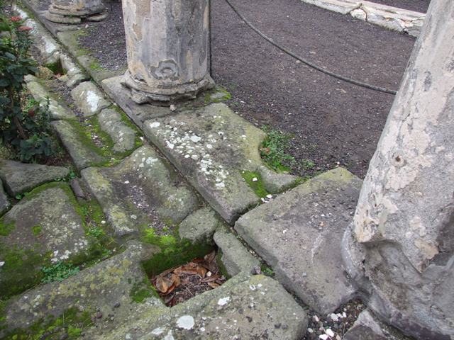 VI.6.1 Pompeii. September 2004. Peristyle, looking east along the south portico. According to Jashemski, the peristyle garden was enclosed on all four sides by an elegant portico. This portico was supported by sixteen stuccoed columns, painted yellow below, white and fluted above.
A cistern puteal stood between the first two columns at the south end of each of the long sides of the portico. Only the puteal on the west side (left in photo above) is preserved.