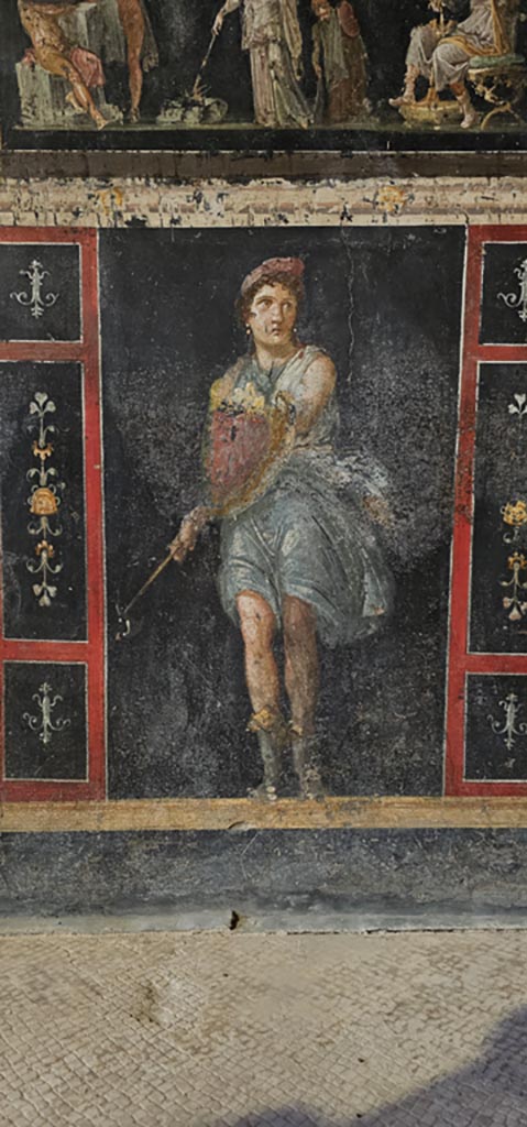 VI.15.1 Pompeii. December 2023. 
Zoccolo on lower west wall on south side of central panel with Amazon holding axe and shield. 
Photo courtesy of Miriam Colomer.

