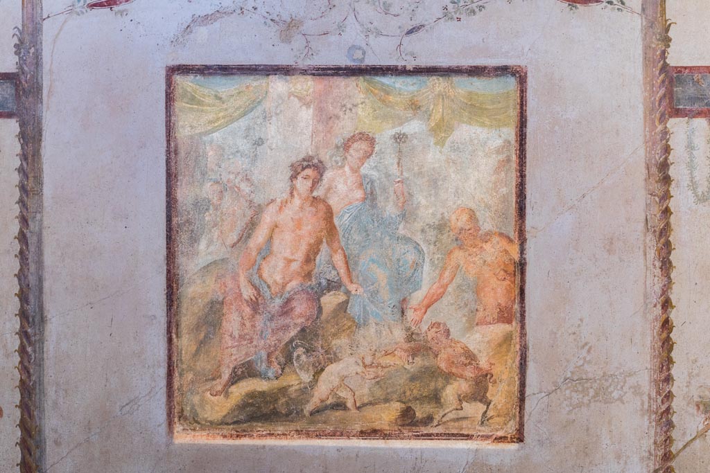 VI.15.1 Pompeii. December 2018.  
Central wall painting on south wall showing Dionysus and Ariadne, as well as the fight between Eros and Pan. Photo courtesy of Aude Durand.
Kuivalainen comments –
“A young half-naked Bacchus in the company of Ariadne, watching the fight about to begin, and Silenus already preparing to reward the victor with the palm leaf. The female figure’s dignified appearance suits Ariadne more than a maenad. His identification is also supported by her embracing arm. This motif of a fight between a cupid and a faun appears elsewhere as well; a good example is an outdoor scene from Herculaneum.” (MANN 9262).
See Kuivalainen, I., 2021. The Portrayal of Pompeian Bacchus. Commentationes Humanarum Litterarum 140. Helsinki: Finnish Society of Sciences and Letters, (p.133-35, D13).

