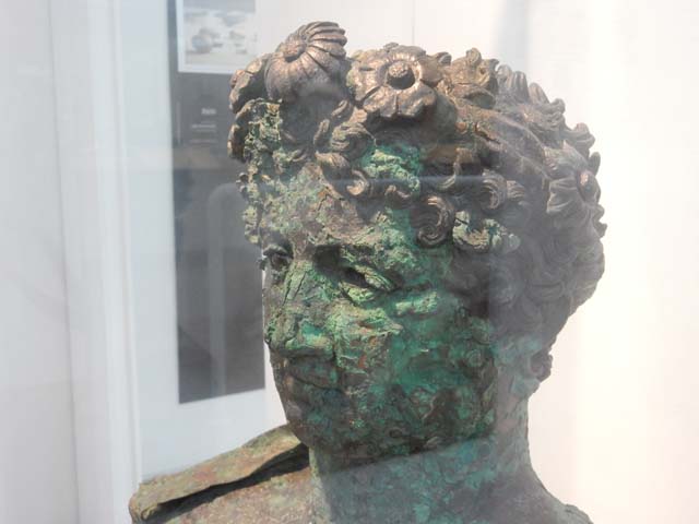 VII.16.17-22, Pompeii. May 2018. Detail of Bronze Herm discovered at Insula Occidentalis.
The hair is made up of a dense mass of short curls and a thin crown adorned with flowers.
Photo courtesy of Buzz Ferebee.
Now in Boscoreale Antiquarium and Museum, inventory number: 13441.
