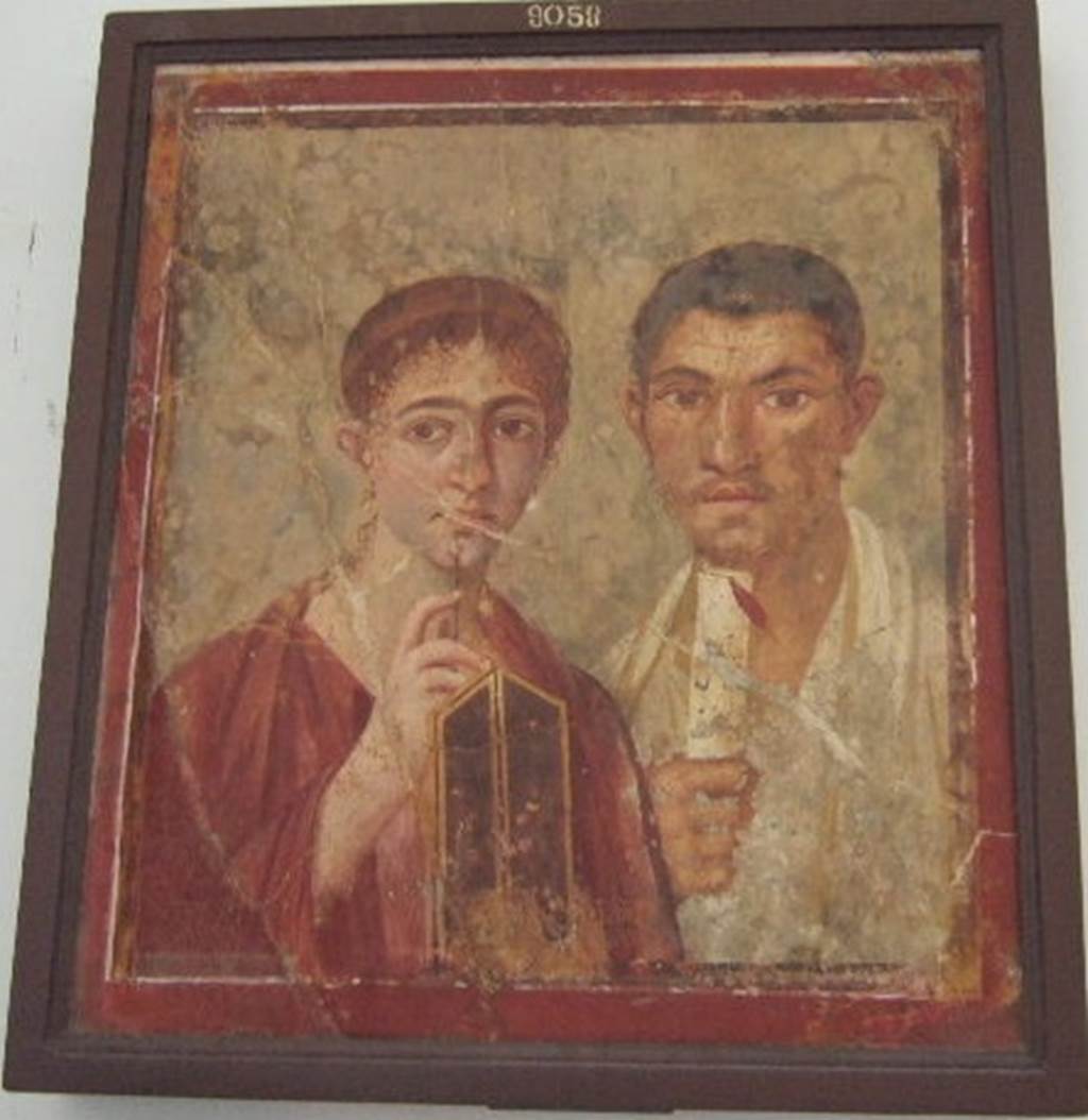 VII.2.6 Pompeii. Portrait of Terentius Neo and his wife. Found on north wall of exedra/tablinum in centre of north side of atrium.  Now in Naples Archaeological Museum.  Inventory number: 9058.
In the upper zone of the painted architecture was a fresco of Cupid and Psyche. The red zoccolo showed a painted plant in the centre panel, and painted garlands with peacocks on them in the side panels. In the middle zone of the wall, the central panel was painted white, which separated the two yellow side panels.
In one of these side panels, but already very faded and nearly vanished was the painting of Nike standing on a shelf, and carrying a trophy on his left shoulder. 
