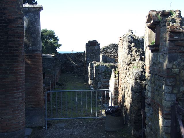 VII.16.1 Pompeii. September 2005. Looking north-west from Temple of Venus towards entrance doorway, on right. On the left behind the wall would have been the area of the portico and peristyle. According to Garcia y Garcia, this house was badly hit by the bombing on 13th September 1943. The bombing totally demolished the atrium, five annexed rooms on the north and east sides, and the portico near the baths. The impluvium has now totally vanished. In many ways, the restoration of 1950 has changed and distorted the original plan of the house. The stairs on the north-west side of the atrium and the portico have vanished. The baths of the house are now accessible only from no.12. Near the baths was a portico of fourteen columns. The portico does not exist anymore, erased by the bombardment.
See Garcia y Garcia, L., 2006. Danni di guerra a Pompei. Rome: L’Erma di Bretschneider. (p.130-1)
According to Jashemski, the peristyle garden was reached by a short flight of steps, at the left west rear of the atrium. It was enclosed by a portico on the south, east and north, supported by columns.
See Jashemski, W. F., 1993. The Gardens of Pompeii, Volume II: Appendices. New York: Caratzas. (p.201)