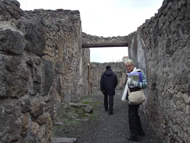 IX.1.7 Pompeii. December 2007. Lararium on south wall of atrium.
According to Boyce,there was a heavy masonry ledge above the panel painted to represent a block of red and yellow variegated marble, bordered in red. It was supported by twin scrolls and ornamented with several bands of stucco relief. On the masonry ledge were the bases of four delicate half-columns, two on each side of an arched niche.
A heavy gable roof used to project from the wall. Within the niche a polychrome stucco cornice runs around the middle of the walls, dividing them into sections, the upper one painted red, the lower one painted blue. On the blue background of the lower section are human figures in stucco relief – now poorly preserved. The arched ceiling is fitted with a shell of stucco. Around the curve of the arch on the wall outside runs another stucco cornice.
See Boyce G. K., 1937. Corpus of the Lararia of Pompeii. Rome: MAAR 14. (p.79, and Pl.6,1). 
