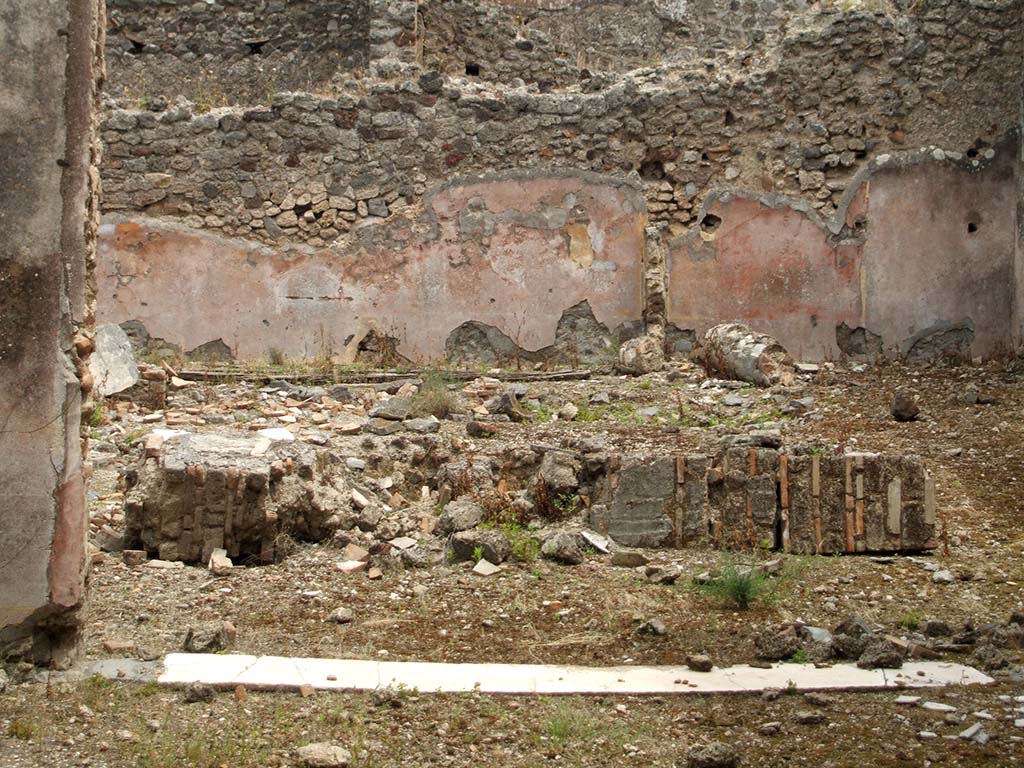 IX.5.18 Pompeii. May 2005. Looking east from triclinium room f, across atrium and pool, in atrium/courtyard b, with remains of a fallen column.
On the east side of the atrium, the rear (east) wall of room k (a narrow storeroom with stairs to the upper floor) can be seen on the left.
On the right, would have been the rear (east) wall of room i, a cupboard with holes for shelving supports.

