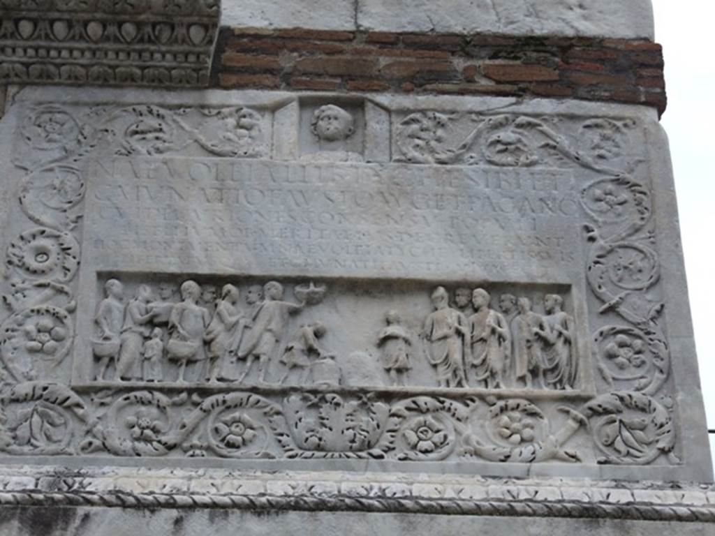 HGW22 Pompeii. December 2007. East side with carving of marble floral pattern, people and inscription.
On the panel above the people is the Latin inscription:

NAEVOLEIA .  L  LIB  TYCHE  SIBI  ET
C. MVNATIO  FAVSTO  AVG  ET  PAGANO
CVI  DECVRIONES  CONSENSV  POPVLI
BISELLIVM  OB  MERITA  EIVS  DECREVERVNT
HOC  MONIMENTVM   NAEVOLEIA  TYCHE  LIBERTIS  SVIS
LIBERTABVSQ  ET  C.  MVNATI  FAVSTI  VIVA  FECIT.

According to Epigraphik-Datenbank Clauss/Slaby (See www.manfredclauss.de) this reads

Naevoleia L(uci) lib(erta) Tyche sibi et
C(aio) Munatio Fausto Aug(ustali) et pagano
cui decuriones consensu populi
bisellium ob merita eius decreverunt
hoc monimentum Naevoleia Tyche libertis suis
libertabusq(ue) et C(ai) Munati Fausti viva fecit      [CIL X 1030]

Mau translated this as:

Naevoleia Tyche, freedwoman of Lucius Naevoleius, for herself and for Gaius Munatius Faustus, member of the Brotherhood of Augustus and suburban official, to whom on account of his distinguished services the city council, with the approval of the people, granted a seat of double width. 
This monument Naevoleia Tyche built in her lifetime also for the freedmen and freedwomen of herself and of Gaius Munatius Faustus.

See Mau, A., 1907, translated by Kelsey, F. W., Pompeii: Its Life and Art. New York: Macmillan. (p. 422-3).