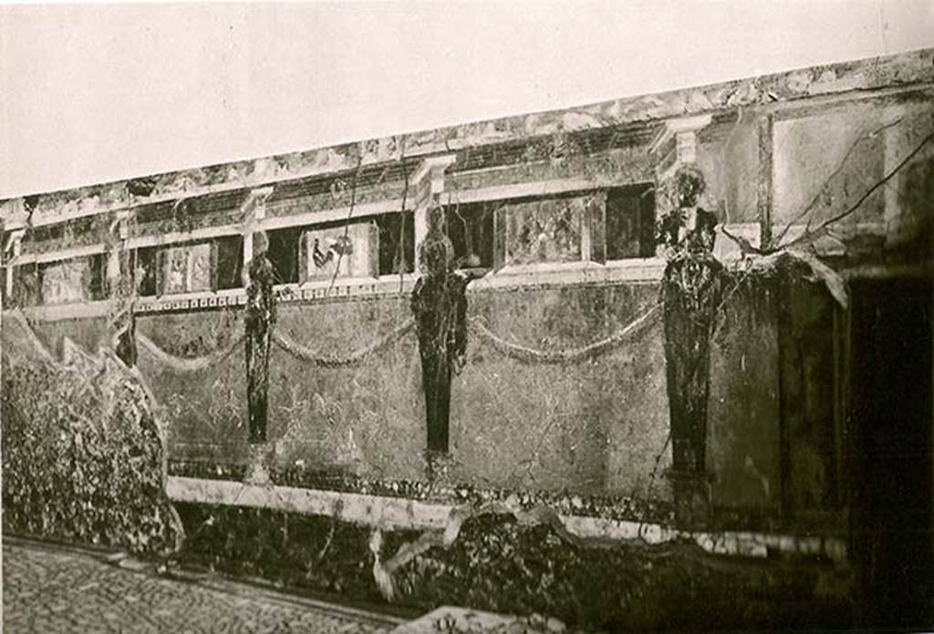 I.6.2 Pompeii. Early 20th C? Old undated photograph of south wall of oecus/triclinium in south-east corner.bRight to left there are four pinax (windowed views with painted shutters).
The Banquet of Silenus.
A Cock with a basket of figs, plums and dates, or which one is on the floor.
The farewell of Alcestis, as she goes to take ferry of Charon to the underworld.
Another still life, but badly preserved.
See La Rocca, de Vos, de Vos, 1981. Guida Archeologica di Pompei; II Edizione. Milano: Arnoldo Mondadori Editore. p. 204.