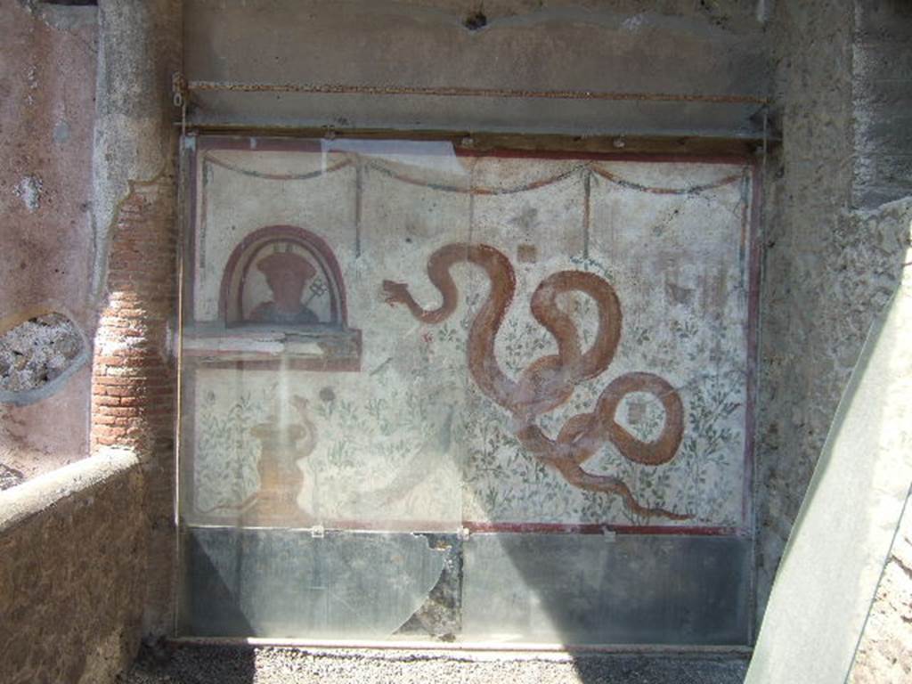 I.6.2 Pompeii. May 2006. Painted lararium on west wall near portico.
Fortunately, the lararium was not damaged by the bombing of 19th September 1943, whereas the nearby portico was destroyed.
According to Boyce, above a black dado there was a white panel marked off by red stripes. On the left side was an arched niche with a projecting ledge beneath it. The bust of Mercury was painted on the rear wall of the niche. On the right side of the white panel there was a large yellow serpent, raising his head to the niche. Below the niche was a second serpent coiling around a yellow cylindrical altar. There were painted green plants with red, yellow and blue flowers, amongst them were two butterflies and three birds. Near the larger serpent there was a peacock standing amongst the plants. Across the top, there were three garlands.
See Boyce G. K., 1937. Corpus of the Lararia of Pompeii. Rome: MAAR 14. (p.25, no.36, pl.9,3)