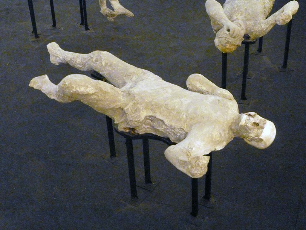 I.6.2 Pompeii. September 2015. Exhibit from the Summer 2015 exhibition in the amphitheatre.
Plaster cast of victim number 20 found to the north of the other group of two females.
Under the abdomen was an iron key and the victim had two rings on the right hand, one bronze, the other iron with an elliptical gem on which was incised the figure of the god Mercury standing left, with purse and caduceus.
See Osanna, N., Capurso, A., e Masseroli, S. M., 2021. I Calchi di Pompei da Giuseppe Fiorelli ad oggi: Studi e Ricerche del PAP 46, p. 362-4.