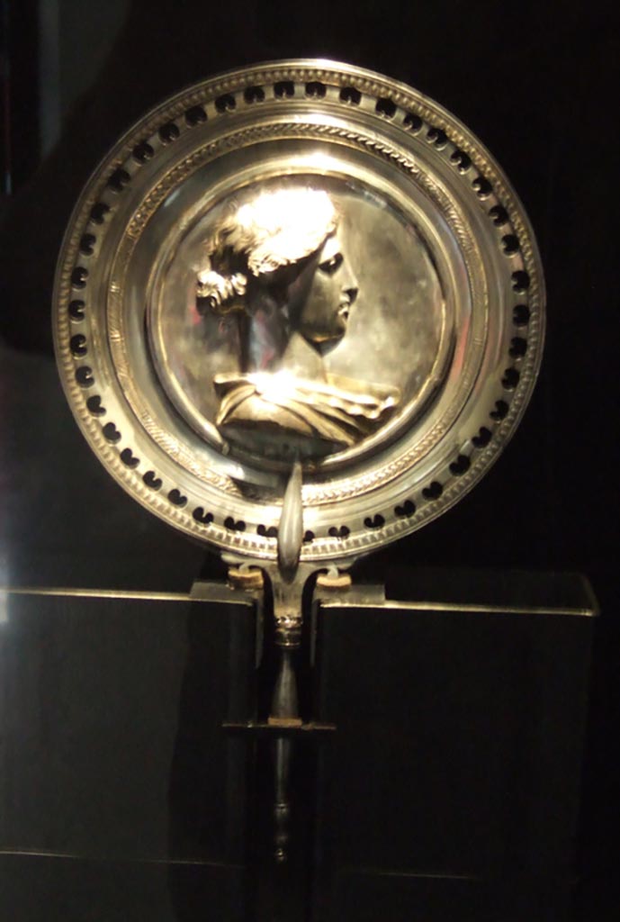 I.10.4 Pompeii. Richly decorated silver mirror with the bust of young woman in the centre.
Part of the 115 pieces of Silver found in a chest in the underground storerooms.
Now in Naples Archaeological Museum. Inventory number 145525.
See Guzzo, P. (A cura di), 2006. Argenti a Pompei. Milano, Electa. p.223.