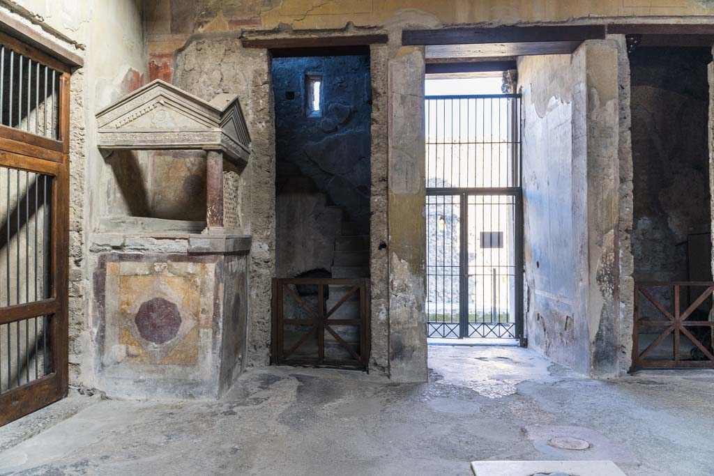 I.10.4 Pompeii. April 2022. Aedicula lararium with stucco decoration, in north-west corner of atrium.
Behind is room 2 with stone stairs to an upper floor. Photo courtesy of Johannes Eber.