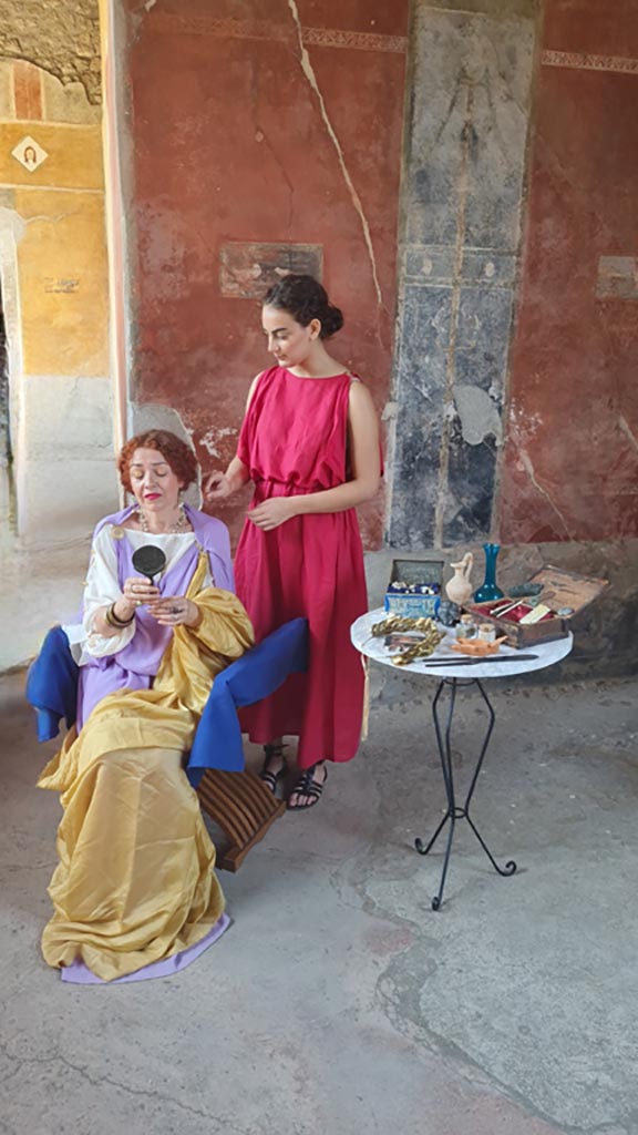 II.3.3 Pompeii. 8th June 2024.
Room 11, north portico, actors portraying slave attending to mistress’s hair and beauty. Photo courtesy of Giuseppe Ciaramella.
Historical reconstruction entitled L’altra Pompei prende vita (The other Pompeii comes to life).