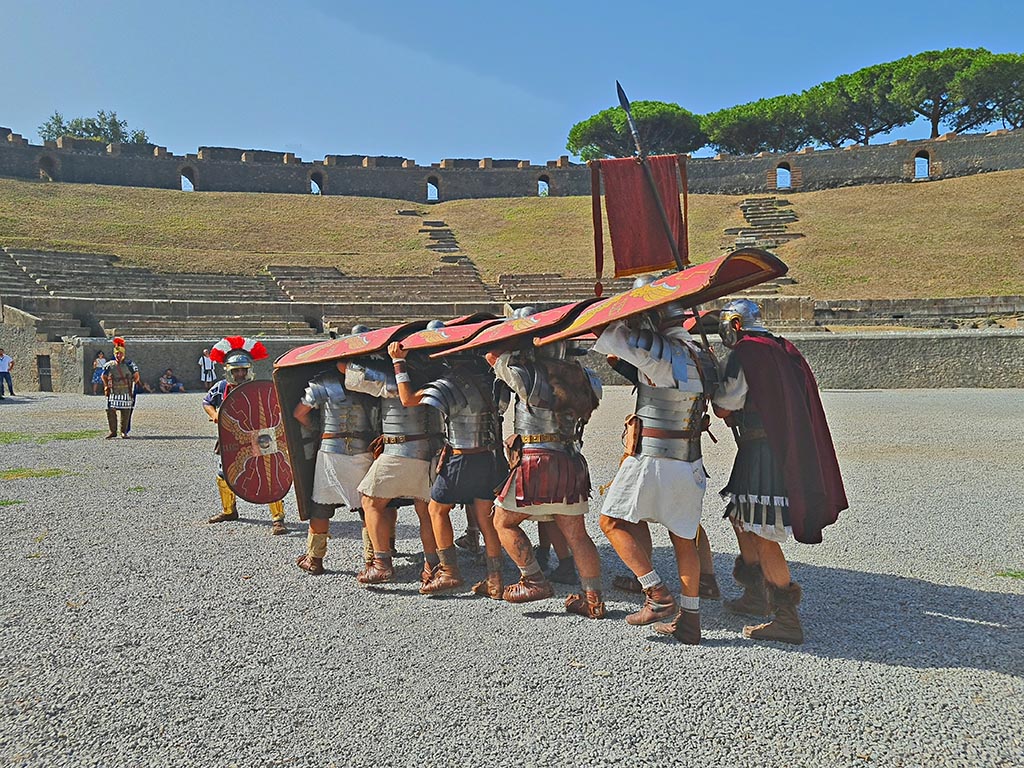 II.6 Pompeii. September 2024. Roman Soldiers – attacking action – testudo/tortoise formation.
This was slow-moving, but almost impenetrable to enemy fire, and thus very effective during sieges and/or when facing off against enemy archers.
Cohorts approached the city's wall in testudo formation, bringing up battering rams and ladders to breach the gates and scale the walls.
However, the testudo formation did not allow for effective close combat – therefore it was used only when the enemy were far enough away.
Photo courtesy of Giuseppe Ciaramella.