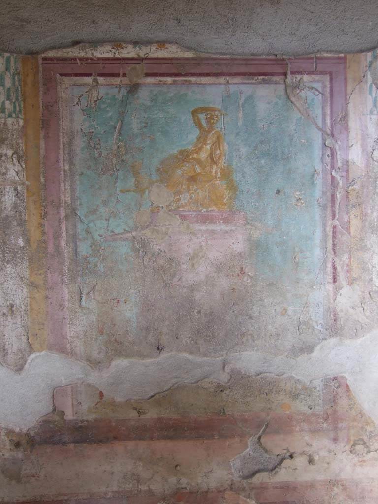 V.1.18 Pompeii. March 2009. East wall of exedra “y”.
Wall painting of Dionysus (or Ariadne?) seated on a pedestal.
See Leach, E.W., 2004. The Social Life of Painting in Ancient Rome and on the Bay of Naples. Cambridge UK: Cambridge UP. (p.135).
According to NdS, it is Bacchus, seated, with his arm on his head and his panther at his feet.
The panther has turned its head towards Bacchus.
See Notizie degli Scavi di Antichità, 1876, p. 79.
Kuivalainen describes this as a composition of three (or four) figures.
In the left corner, a naked male carries a sack or a wineskin in his left hand. In the middle stands a wreathed Silenus with several wineskins on the ground. (There may be a third figure between these two.)
The red pedestal with white details is decorated with garlands; on top of the pedestal, on a bench covered with a cloth and a thick pillow, reclines an effeminate youth; his body is golden yellow with reddish shades and white reflections; his right arm is raised on top of his head, turned left, wreathed and with two small horns; he holds a cantharus in his hand, in his left arm he has a thyrsus pointed downwards and a tympanum; he wears a thin cloak, which covers his legs, and a nebris tied over his left shoulder.
Behind his knees peeks a panther, standing with his left foreleg raised. Trees are painted across the background.
Kuivalainen comments –
Bacchus is depicted as a gilded bronze statue. The effeminate features and small breasts are typical for a young Bacchus with horns, but the tympanum as his personal attribute is rare. The reference to the Anthesteria is theoretical, with wine skins as the only references, nor does the pictorial programme with its plethora of paintings in the room support this interpretation, as the paintings are rather linked to Bacchus and Venus.
See Kuivalainen, I., 2021. The Portrayal of Pompeian Bacchus. Commentationes Humanarum Litterarum 140. Helsinki: Finnish Society of Sciences and Letters, p.185.
(Note: in his Bibliography he quotes – Dilthey 1876, 311-313, (AdI): Effeminate Bacchus, with a similar statue found in Herculaneum (MANN 9276), a drinking contest in the Anthesteria festival in Athens.)