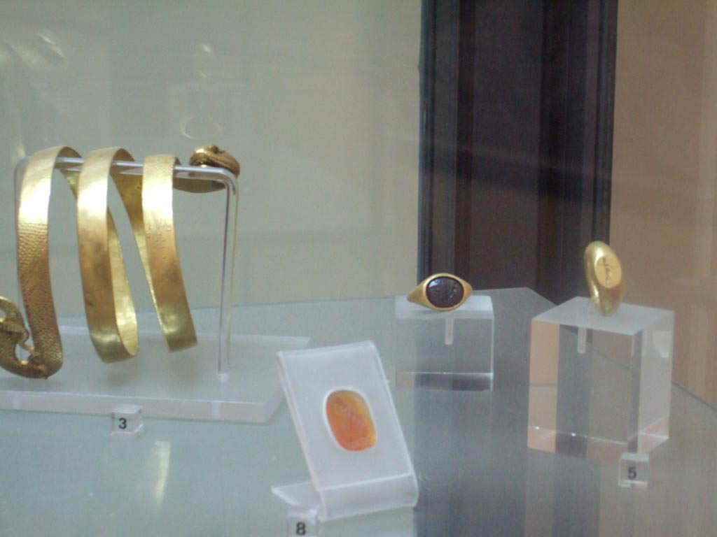 VI.12.2 Pompeii. Found 4th March 1831. Jewellery found in VI.12.2.
Carving on cornelian of bust of a youth, possible Alexander the Great (in front). Inventory number 26766.
Gold ring with oval centre representing Hercules in the garden of Hesperides (on right). Inventory number 25132.
Gold ring with nude figure, with discus/shield and javelin (at rear). Inventory number 25084.
Now in Naples Archaeological Museum.