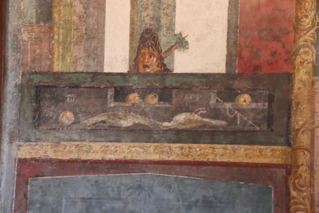 VI.15.1 Pompeii. October 2023.
Detail of panel from east wall at north end, with wall painting of food with mask above. Photo courtesy of Klaus Heese.
