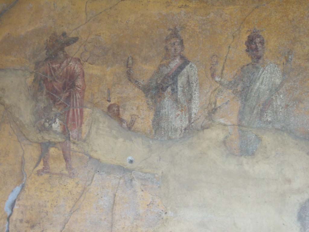 VI.16.7 Pompeii. May 2006. Room F, painting of gods on the south wall of the peristyle.
Isis is in the centre wearing a red and black sash and holding a sistrum.
Anubis is dressed in red. A small figure between Isis and Anubis is possibly Harpocrates.
Serapis or Osiris is dressed in white with the horn of plenty in his left hand and a sistrum in his right.
See Fröhlich, T., 1991. Lararien und Fassadenbilder in den Vesuvstädten. Mainz: von Zabern. (L74, T. 38,1-2).