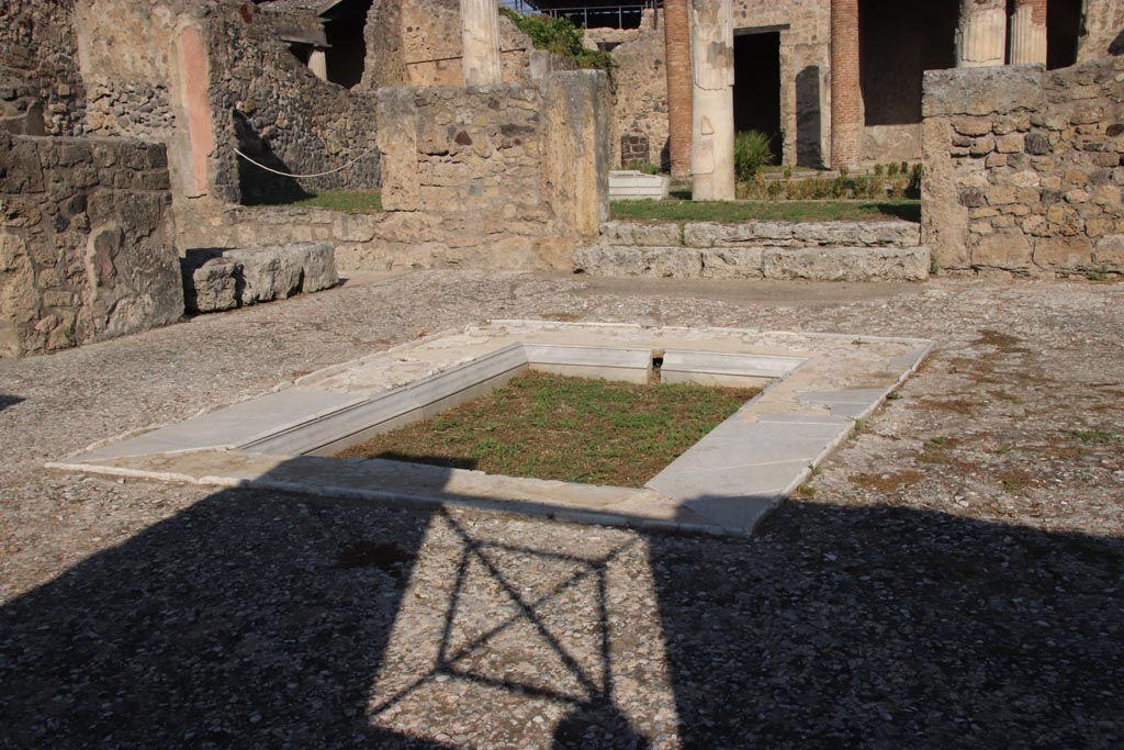 VII.7.5 Pompeii. October 2023.
Looking north-west across impluvium in atrium towards west ala (e ), on left. Photo courtesy of Klaus Heese.