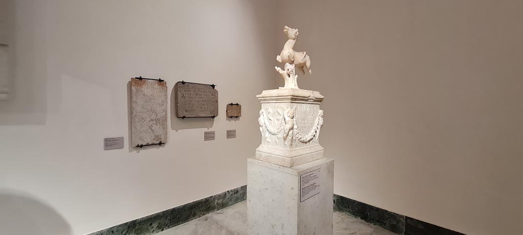 VII.7.32 Pompeii. April 2023. Looking towards a statuette on a base in a corner of “Campania Romana” gallery.
At the rear on the wall are Dedications found in the Temple. Photo courtesy of Giuseppe Ciaramella.