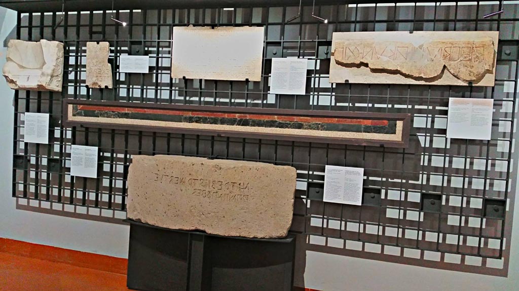 VII.7.32 Pompeii.
Centre of photo, part of red and green/black floor mosaic with epigraph, on display in Naples Archaeological Museum, inv. 113398.
Ovius Campanius … quaestor, by decree of the assembly, with the money of Apollo… had (this) made.
The inscription, in Oscan written from right to left, refers to the restoring of the floor of the Temple of Apollo with the money of the offerings of the faithful.
Photo courtesy of Giuseppe Ciaramella, June 2017.