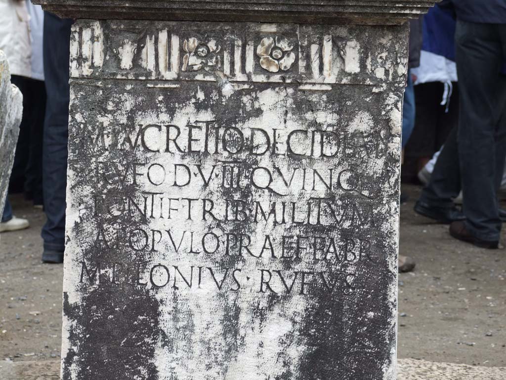 VII.8 Pompeii Forum. May 2010. Pedestal base for statue, decorated with bull's heads and flower motifs. This has the Latin inscription –

M .  LVCRETIO . DECIDIAN
RVFO . D . V. III . QVINQ
PONTIF . TRIB . MILITVM
A POPVLO . PRAEF . FABR
M . PILONIVS . RVFVS

See Pappalardo, U., 2001. La Descrizione di Pompei per Giuseppe Fiorelli (1875). Napoli: Massa Editore. (p. 101)

According to Pagano and Prisciandaro, this was found in June 1816, it read –

M(arco) Lucretio Decidian(o)
Rufo d(uum)v(iro) III quinq(uennali)
pontif(ici) trib(uno) militum
a populo praef(ecto) fabr(um)
M(arcus) Pilonius Rufus     [CIL X 788]

See Pagano, M. and Prisciandaro, R., 2006. Studio sulle provenienze degli oggetti rinvenuti negli scavi borbonici del regno di Napoli. Naples: Nicola Longobardi.  (p.114)   
PAH III, 7.

According to Cooley, this translates as

To Marcus Lucretius Decidianus Rufus, duumvir three times, quinquennial, priest, military tribune by popular demand, staff officer. Marcus Pilonius Rufus set this up.

See Cooley, A. and M.G.L., 2004. Pompeii: A Sourcebook. London: Routledge. F92, 0. 130.

