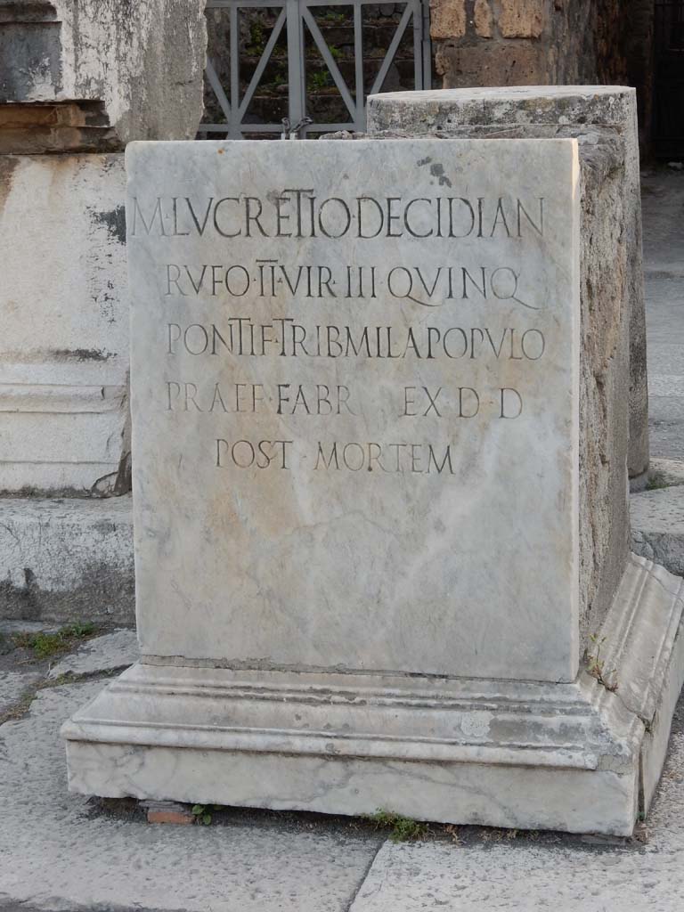 VII.8 Pompeii Forum. June 2019. Pedestal base for statue. Photo courtesy of Buzz Ferebee. This has the Latin inscription –
M . LVCRETIO . DECIDIAN 
RVFO . II . VIR . III . QVINQ
PONTIF . TRIB . MIL .  A POPVLO
PRAEF . FABR . EX . D . D
POST . MORTEM
See Pappalardo, U., 2001. La Descrizione di Pompei per Giuseppe Fiorelli (1875). Napoli: Massa Editore. (p. 101)
According to Pagano and Prisciandaro, this was found in June 1816, it read –
M(arco) Lucretio Decidian(o)
Rufo IIvir(o) III quinq(uennali)
pontif(ici) trib(uno) militum a populo
praef(ecto) fabr(um) ex d(ecreto) d(ecurionum) post mortem       [CIL X 789]
See Pagano, M. and Prisciandaro, R., 2006. Studio sulle provenienze degli oggetti rinvenuti negli scavi borbonici del regno di Napoli. Naples: Nicola Longobardi, (p.114)   PAH III, 7.
According to Berry, Marcus Lucretius Decidianus Rufus had a particularly distinguished career.  The inscription on his statue reads –
To Marcus Lucretius Decidianus Rufus, three times duumvir, (once as) quinquennial duumvir, priest, military tribune by popular decree, military aide-de-camp, in accordance with a decree of the decuriones after his death (CIL X 789)
See Berry, J., 2007. The Complete Pompeii. London: Thames & Hudson. (p.133)

