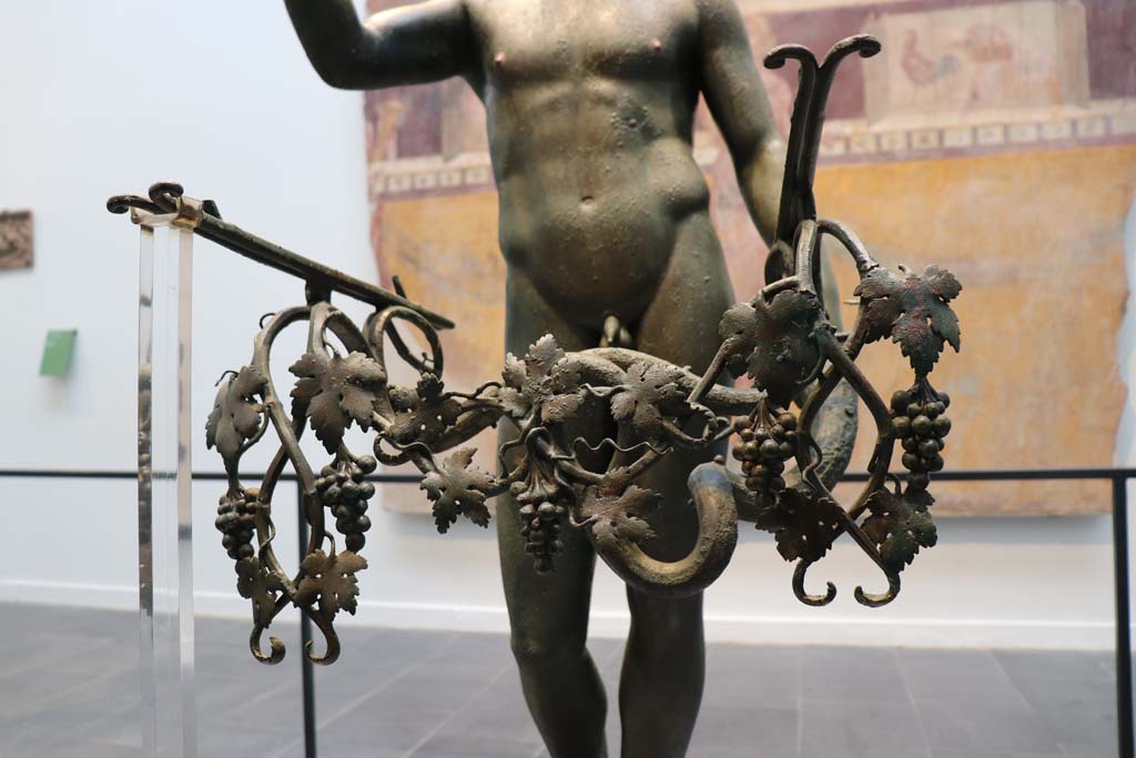 VII.16.17-22 Pompeii. February 2021.
Detail of the addition of bunches of grapes on a vine to the statue of the bronze Ephebus, used as an oil lamp holder, found in dining room.
Photographed on display in Antiquarium. Photo courtesy of Fabien Bièvre-Perrin (CC BY-NC-SA).
