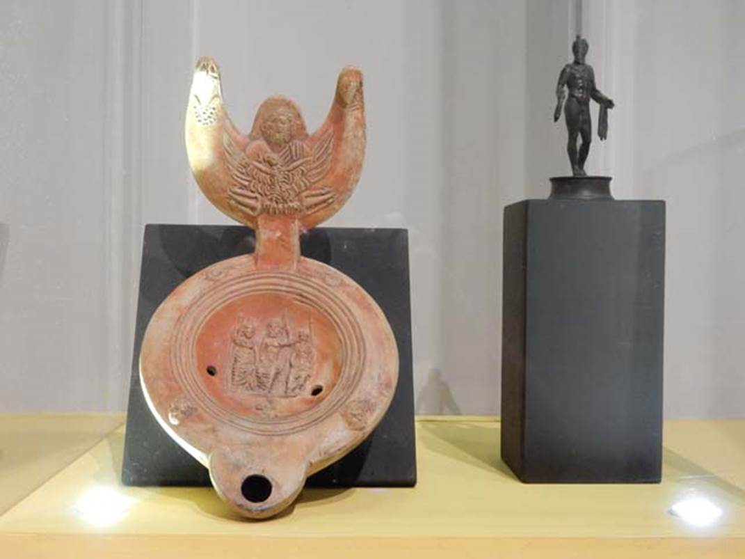 VII.16.17-22, Pompeii. May 2018. Oil lamp, with Jupiter and Eagle on the handle, and Jupiter, Juno and Minerva in the central part.
Parco Archeologico di Pompei, inventory number 13962.
Bronze statuette of Mercury holding a sack of coins, Parco Archeologico di Pompei, inventory number 13987.
Photo courtesy of Buzz Ferebee.