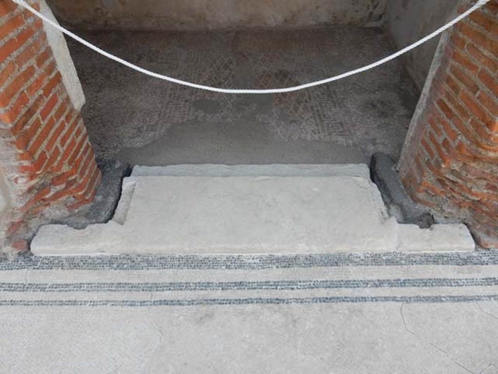 VIII.2.16 Pompeii. May 2017. Threshold to doorway of cubiculum in centre of south wall of atrium. Photo courtesy of Buzz Ferebee.
The indents in the limestone threshold clearly show that the doorway was fitted with wooden door-jambs and that its doors opened inside the room, where the floor decoration clearly defined the anticamera and the bed alcove. The floor is seen with a “carpet” outline of white tesserae in a diamond shaped net design with a border of meanders alternating with squares and a central tessera.