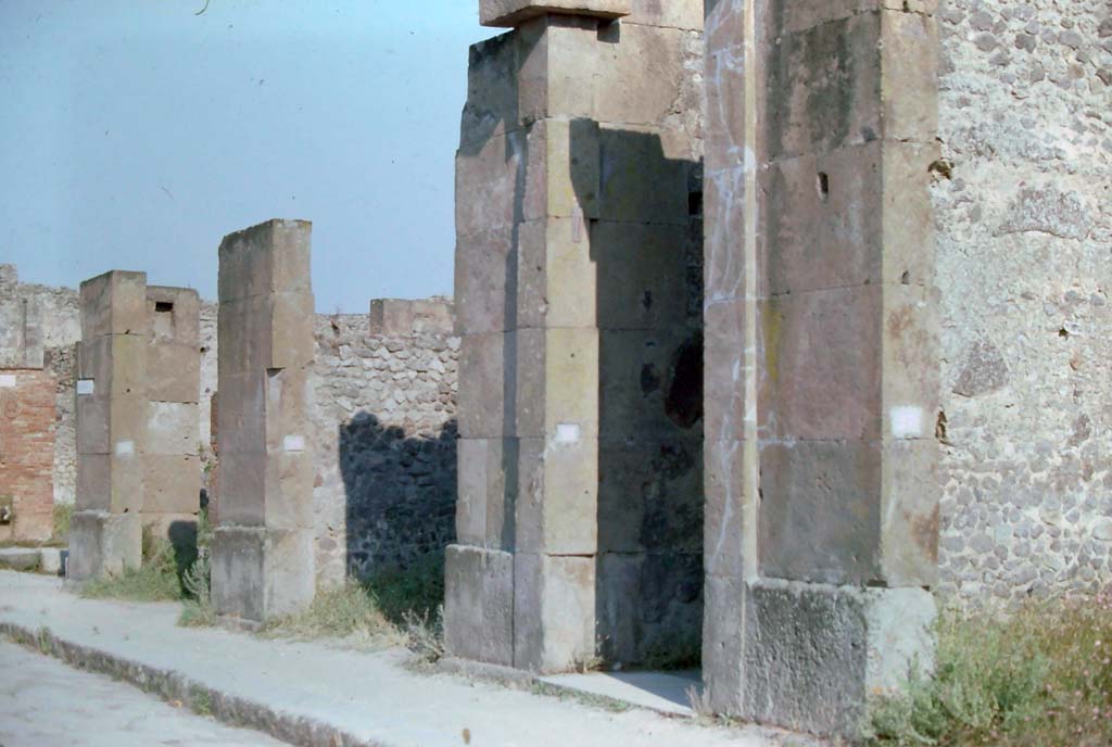 VIII.5.28 Pompeii. 7th August 1976.
Looking south-east along south side of Via dell’Abbondanza, with Via dei Teatri, on left, followed by VIII.5.30/29/28 and 27, on right.
Photo courtesy of Rick Bauer, from Dr George Fay’s slides collection.
According to Bonucci,
Casa di Fusco – 1819 - Before arriving to the Piazza del Teatro you pass by an infinite number of shops, which attest trade, and the riches of this city. Among them we can recognize, from their exhibition, those where the mosaicists worked. The fountains with beautiful quadrangular marble basins are abundant in this street. Their abundance, and that of wells, reservoirs, and cisterns, as well as the universal use of baths, public and private gardens, and galleries open to the sea attest to the great heat which suffer on this volcanic hill, and the well-understood measures taken to guarantee it. On this street a glass vase with whole eggs was found; and 939 bronze coins.
Fusco's house has a beautiful Gynaeceum, mosaics, and the varied and ingenious decorations in the capricious taste of a stage performer. Fish are depicted in the dining room, and love scenes in the bedroom. Not a few bronze, glass, and terracotta vases were found; two gold pendants, and a piece of pitch, which after so many centuries still retains the smell of that substance.
See Bonucci, C., 1827. Pompei Descritta: Terza Ed. Napoli: Miranda, p. 177.