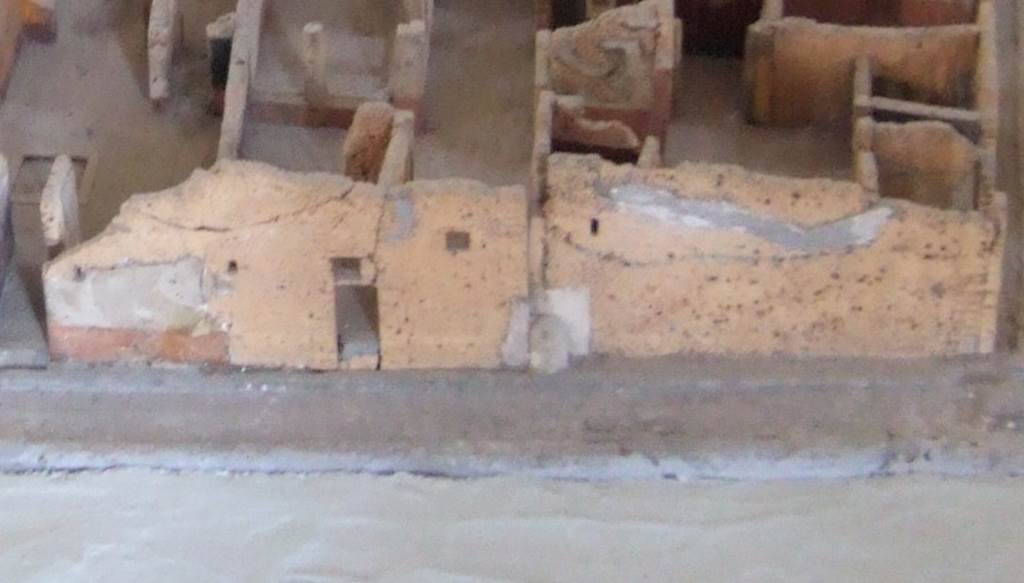 IX.2.19 Pompeii. Street shrine on west side of Vicolo di Tesmo, as shown on model in Naples Archaeological Museum. According to Trendelenburg in BdI, “not far from the north-east corner (of insula IX.2) the wall makes an angle. By this angle was a buttress of material elevated to the height of I.40m from the ground. Above this, one looked on the head of a warrior near to natural size and painted in a very coarse manner. The formidable figure, his armour of crested helmet, shield, lance and breastplate would have given a real surprise to those who came across him unexpectedly. I do not know precisely if this was not the purpose of his warlike face, to intimidate and drive away those “moratores otiosi”, that the solitude of the corner would attract”. “Moratores otiosi” could be translated as loafers, vagrants, undesirables hanging around the area.
See Trendelenburg in BdI, 1871, (p.194)