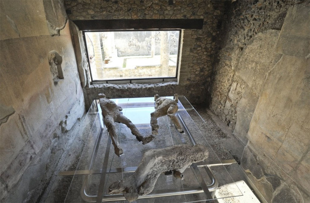 VII.1.47 Pompeii. March 2017. Room 8, looking across plaster-casts towards window in east wall.
Plaster-cast of victim 2 can be seen in the lower part of the photograph.
The fractured remains were badly hit by the 1943 bombing of the Antiquarium.
In this photo, she is seen lying with her head to the right, whereas in the Sommer and Behles photo, above, she is lying with her head to the left.
They were found in the Vicolo degli Scheletri.