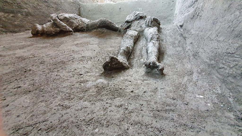 
November 2020. The bodies were found in a side room of the cryptoporticus.
The plaster casts have yielded the shapes of the bodies of the two victims, in a supine position, victim 92 (right) and victim 93 (left). 

Both had died suddenly during the so-called second pyroclastic flow, which struck Pompeii and the surrounding area in the early hours of the 25th October, leading to the death of the survivors who were still present in the city and countryside. This second flow was preceded by a brief period of quiet, perhaps half an hour, during which the survivors both at Pompeii and probably at Cività left their dwellings in a vain attempt to save themselves.

The flow that struck was however very fast and very violent, bringing down the first floors of the houses and surprising the victims as they attempted to escape across a few centimetres of ash, leading to their deaths. In this case it is probable that the pyroclastic flow flooded the room through several openings, entombing them in the ash.

Novembre 2020. I corpi sono stati individuati in un vano laterale del criptoportico.
I calchi in gesso hanno prodotto le forme dei corpi delle due vittime, in posizione supina, vittima 92 (a destra) e vittima 93 (a sinistra).. 

Entrambe erano state sorprese dalla morte durante la cosiddetta seconda corrente piroclastica, che nelle prime ore del mattino del 25 ottobre investì Pompei e il territorio circostante portando alla morte dei superstiti ancora presenti in città e nelle campagne. Questa seconda corrente era stata preceduta da una fase di breve quiete, forse di una mezz’ora, durante la quale i sopravvissuti sia a Pompei che probabilmente a Civita, uscirono dalle abitazioni nel vano tentativo di salvarsi.

La corrente che lì investì fu però molto veloce e turbolenta abbatté i primi piani delle abitazioni e sorprese le vittime mentre fuggivano su pochi centimetri di cenere, portandoli alla morte. Nel nostro caso è probabile che la corrente piroclastica abbia invaso l’ambiente da più punti inglobando e seppellendole nella cenere.

Photograph © Parco Archeologico di Pompei.

