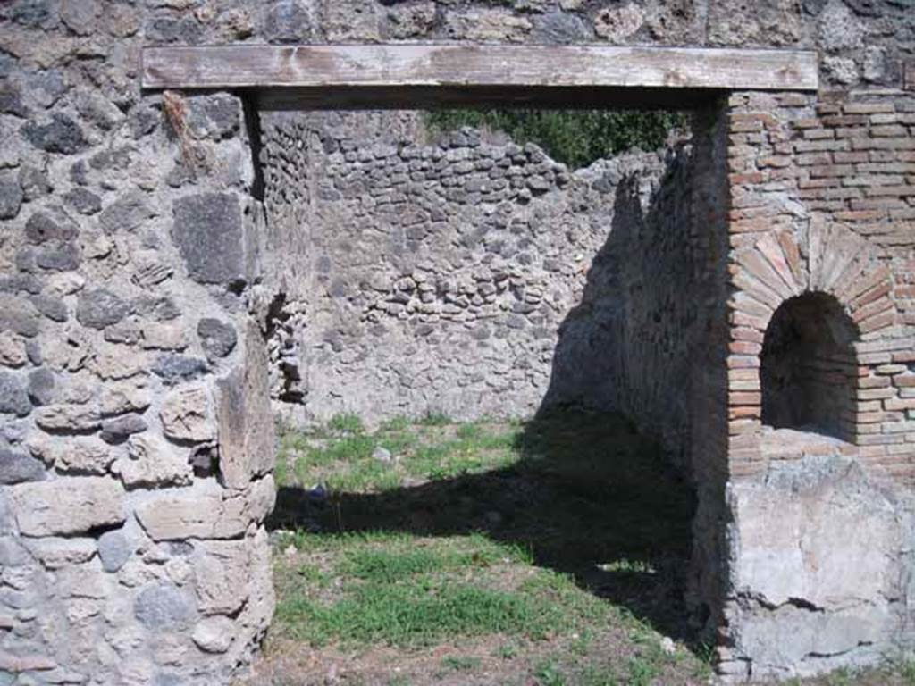 I.1.2 Pompeii. September 2010. 
Doorway to rear room "b"  in north-east corner, perhaps for the use of customers. 
Looking east. Photo courtesy of Drew Baker.

According to Warscher, quoting Mau in Bull. Inst 1875, p.26, 
“Dietro alla bottega a destra vi è la spaziosa cucina con focolare e cesso, a sinistra una stanza larga 2,96, profonda 5,24, dipinta negligentemente nello stile degli ultimi tempi di Pompei: i colori predominanti sono rosso nello zoccolo, giallo nella parte media, bianco in quella superiore.  
Sul muro di S troviamo un quadro alto 0,30, largo 0,40, rappresentante la morte di Elle.  Il fondo è tutto riempito di color turchino che rappresenta il mare. Sull’ariete che corre verso destra, sta seduto Frisso, rivolto allo spettatore e la coscia destra, come pare, coperta d’una veste bianca, tenendosi colla sinistra al collo dell’ariete, mentre stende la destra ad Elle, che dietro l’ariete affonda nel mare, alzando verso il fratello ambedue le mani.
Sul muro di E un altro quadro molto mal conservato, alto 0,38, ed altrettanto largo, ci mostra Apolline ritto in piede e rivolto a sinistra, verso la qual parte stende la man destra, mentre sopra la spalla sinistra molto svanita ma con sufficiente vertezza si scorge la lira.  La posizione elevata della lira ed il confronto delle pitture 180 e 201 (helbig) ci lasciano supporre, che essa fosse appoggiata sopra una base o un pilastro. Dal movimento del braccio destro si potrà conghietturare, che nella parte sinistra del quadro fosse ancora un’altra figura, alla quale il deo si rivolgesse”.
See Warscher T., 1936. Codex Topographicus Pompeianus: Regio I.1, I.5. Rome: DAIR, whose copyright it remains. (a, dopo no.11)
(translation:
Behind the shop to the right there was the spacious kitchen with hearth and toilet, to the left a room 2,96 wide, by 5,24 deep, carelessly painted in the style of the last days of Pompeii: the predominant colours were red on the zoccolo, yellow in the middle part, white at the top. On the south wall, a painting of the death of Helle, O,30 high, 0,40 wide, could be seen. The bottom was all filled with blue color representing the sea.
On the ram that moved to the right sat Phrixus, facing to the viewer and the right thigh, as it seemed, covered in a white robe, keeping his left hand around the neck of the ram, while extending the right hand to Helle, who behind the ram sinks into the sea, raising both hands to her brother.  On the east wall, there was another picture very poorly preserved, 0,38 high, and equally wide, showing Apollo standing and turned to the left, extending his right hand, whilst over the left shoulder, very faded but with sufficient to perceive the lyre. The elevated position of the lira and the comparison of paintings 180 and 201 (Helbig) suggested that it was placed above a base or a pillar. By the movement of his right arm, which may be conjectural that on the left side of the picture was yet another figure, to whom the god turned. The execution of both paintings as far as the bad conservation allows us to judge, seemed rather neglected, by the fact that they were overlapping onto the yellow of the wall, whether to execute a painting with greater diligence for the most, or put fresh plaster on after you finish the decorative part of the wall, or at least leave space for it."



