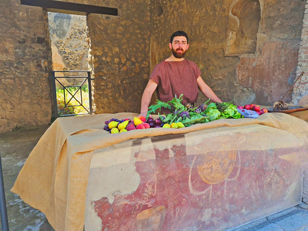 I.8.1 Pompeii. 8th June 2024. 
Looking across counter towards south-west corner and niche in west wall. Photo courtesy of Giuseppe Ciaramella.
Historical reconstruction entitled L’altra Pompei prende vita (The other Pompeii comes to life).
