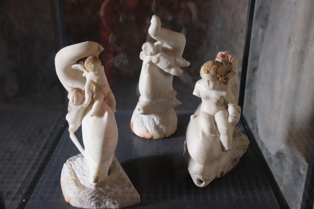 I.9.14 Pompeii. October 2022.
Room 5, display cabinet with three of the four cupids, found in tablinum, room 6. Photo courtesy of Klaus Heese.