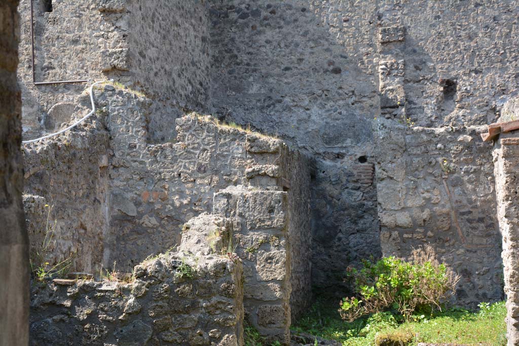 I.10.18 Pompeii. April 2017. Looking south-west from entrance fauces. Photo courtesy Adrian Hielscher.
“Along the south side (of the atrium 1) which was the wall next to the rustic quarters of the Casa del Menandro, a block of limestone was found, which would have been used as reinforcement for the wooden stairs that led up to the upper floor, of which one could see the outline in the plaster.
The “understairs”, closed towards the atrium by a wooden partition, had the two brick walls covered in simple white plaster.

On the west side of the atrium opened, respectively to the right and to the left, 
- a large doorway opening into a room all open to the west (no.6) and defended only by a low wall, covered by canopy/roof,
- and with another room (no.7) of elongated trapezoidal shape, whose south wall, slanting, marks a tilt of the perimeter wall.
In the room to the right, (no.6) there is no trace of the original flat roof cover other than the two large holes of the lintel, there is, on the left side, a recess in the wall, to which a pile of lime had been attached and on the right side were the two limestone blocks, supporting an attached ladder. The flooring was of a simple floor of beaten material; the walls were covered with rustic white plaster, which did not have any decoration.

From here we pass by means of a door rather wide, but occupied in part by the circular mouth of the cistern, into a narrow and long area (no.8), uncovered, with a floor of cocciopesto, onto which poured the dripping of the roofs of this part of the house.
This area (no.8) gave access to the room described as the kitchen (no.9), and at the rear of no.8 was the latrine (no.10), which would have consisted of the usual seat with a recess in the wall for it. 
On the back wall, two low masonry podiums are attached, the second of which was connected to a square base built in the corner.

Along the left side of the walkway (No.8), opened the kitchen, also rectangular and at a lower level than the walkway/yard. The hearth is in the SE corner opposite the entrance, with masonry bench (1.25 m x 0.86 x 0.86) and edges covered with bricks and tiles, on the south wall beyond the podium was the Lararium painting (0.35m x 1.10), preserved only for half of its length, on a white background framed by a red band.
In front of the kitchen was a very small rectangular uncovered area of a few square metres and bordered by a low wall, and in which poured the rainwater from the surrounding roofs.”
See Notizie degli Scavi, 1934, (p.341-4).
According to Allison –
The kitchen, room 9, had coarse plaster on its east and south walls and a tiled floor. On the south wall beside the masonry bench is the lararium painting (preserved for the height of I.8m).
The latrine, room 10, had coarsely plastered walls. The excavators recorded the remains of a wooden seat-plank in the wall, at the south end. 
Its proximity to the kitchen suggests its additional use for general waste.
See Allison, P.M. (2006). The Insula of the Menander at Pompeii: Vol. III The finds, Clarendon Press, Oxford, (p.369-70).  


