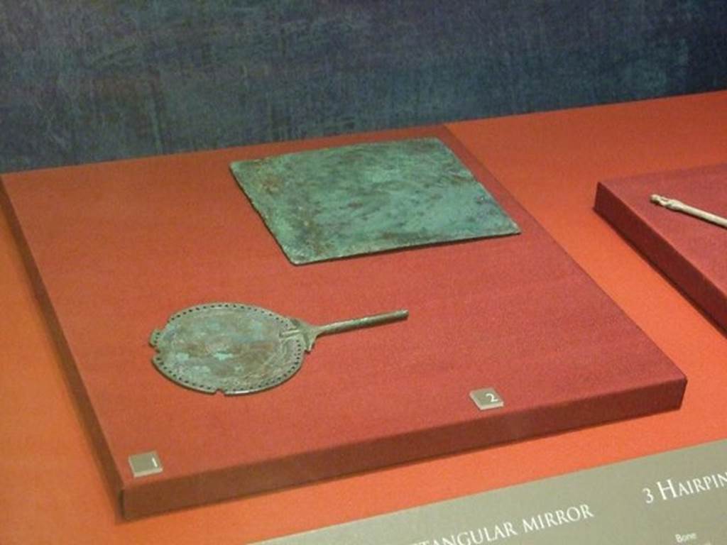 I.11.6 Pompeii. Round silver and bronze mirror (at front). SAP 10790.
Found in a bronze arca (chest) in the south-east corner of the atrium.
Photographed at “A Day in Pompeii” exhibition at Melbourne Museum. September 2009.
According to Mileti, two bronze rings and female toilet items found demonstrated that the house was inhabited at the time of the eruption, also by a woman.
See Mileti, M. C., 2000. La casa I, 11, 6-7 a Pompeii: Rivista di Studi Pompeiani XI, p. 110.
