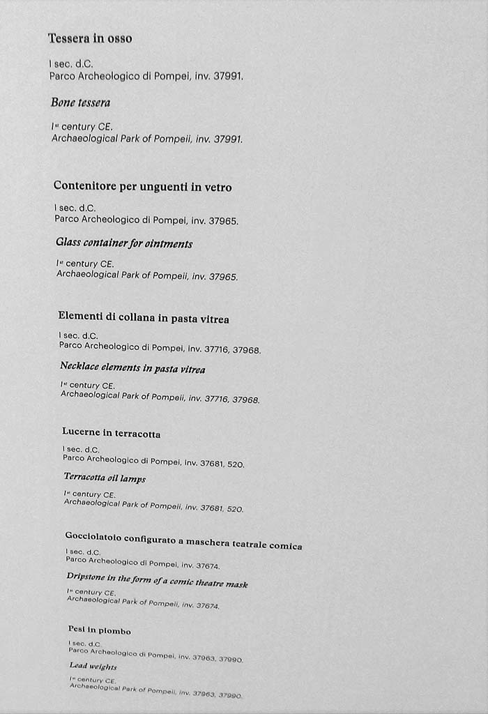 II.9.4 Pompeii. May 2018. Room 8, display list. Photo courtesy of Buzz Ferebee. 
Bone tessera (Tessera in osso), inv.no. 37991
Glass container for ointments (Contenitore per unguenti in vetro), inv.no. 37965
Necklace elements in pasta vitrea (Elementi di collana in pasta vitrea), inv.no. 37716, 37968
Terracotta oil lamps (Lucerne in terracotta), inv.no. 37681, 520
Dripstone in the form of a comic theatre mask (Gocciolatoio configurato a maschera teatrale comica), inv.no. 37674
Lead weights (Pesi in piombo), inv.no. 37963,37990
All inventory numbers from Archaeological Park of Pompeii.
