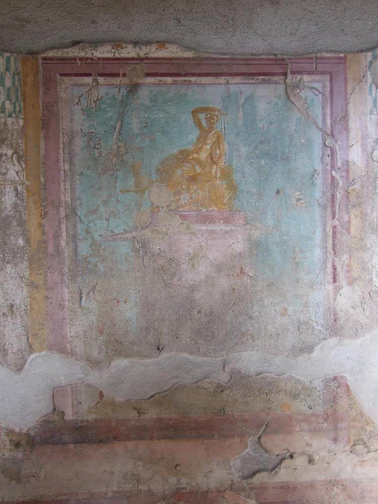 V.1.18 Pompeii. March 2009. East wall of exedra “y”.  
Wall painting of Dionysus (or Ariadne?) seated on a pedestal.
See Leach, E.W., 2004. The Social Life of Painting in Ancient Rome and on the Bay of Naples. Cambridge UK: Cambridge UP. (p.135).
According to NdS, it is Bacchus, seated, with his arm on his head and his panther at his feet.
The panther has turned its head towards Bacchus.
See Notizie degli Scavi di Antichità, 1876, p. 79.
Kuivalainen describes this as a composition of three (or four) figures. 
In the left corner, a naked male carries a sack or a wineskin in his left hand. In the middle stands a wreathed Silenus with several wineskins on the ground. (There may be a third figure between these two.)
The red pedestal with white details is decorated with garlands; on top of the pedestal, on a bench covered with a cloth and a thick pillow, reclines an effeminate youth; his body is golden yellow with reddish shades and white reflections; his right arm is raised on top of his head, turned left, wreathed and with two small horns; he holds a cantharus in his hand, in his left arm he has a thyrsus pointed downwards and a tympanum; he wears a thin cloak, which covers his legs, and a nebris tied over his left shoulder. 
Behind his knees peeks a panther, standing with his left foreleg raised. Trees are painted across the background.
Kuivalainen comments –
Bacchus is depicted as a gilded bronze statue. The effeminate features and small breasts are typical for a young Bacchus with horns, but the tympanum as his personal attribute is rare. The reference to the Anthesteria is theoretical, with wine skins as the only references, nor does the pictorial programme with its plethora of paintings in the room support this interpretation, as the paintings are rather linked to Bacchus and Venus.
See Kuivalainen, I., 2021. The Portrayal of Pompeian Bacchus. Commentationes Humanarum Litterarum 140. Helsinki: Finnish Society of Sciences and Letters, p.185.
(Note: in his Bibliography he quotes – Dilthey 1876, 311-313, (AdI): Effeminate Bacchus, with a similar statue found in Herculaneum (MANN 9276), a drinking contest in the Anthesteria festival in Athens.)
