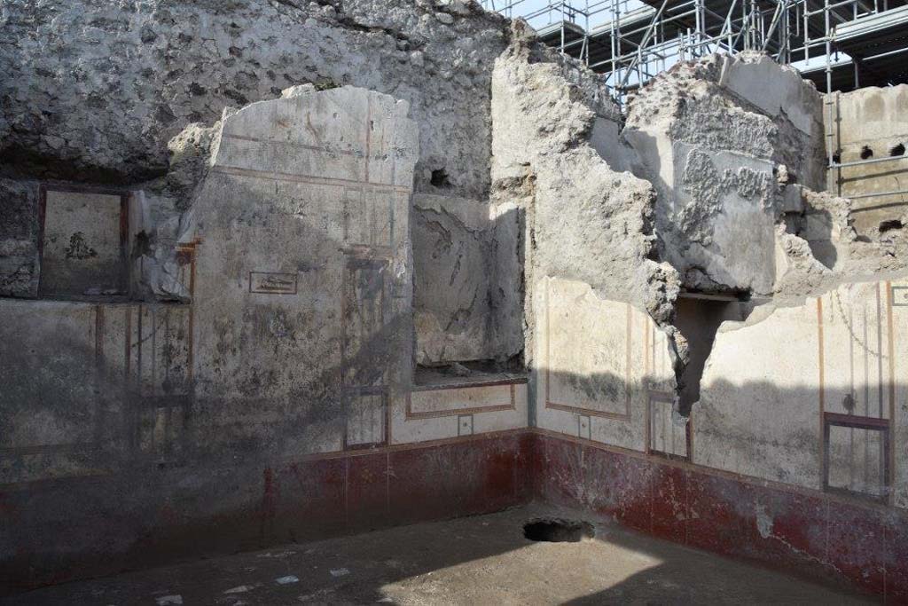 V.3 Pompeii. Casa del Giardino. October 2018. Ambiente 7. West wall with white walls, architectural painting and two niches. Below is a red zoccolo with plants. The north wall is to the right with the square niche of ambiente 8 behind.
Ambiente 7. Parete ovest con pareti bianche, pittura architettonica e due nicchie. Sotto c'è uno zoccolo rosso con piante. La parete nord è a destra con la nicchia quadrata dell'ambiente 8 dietro.
Photograph © Parco Archeologico di Pompei.