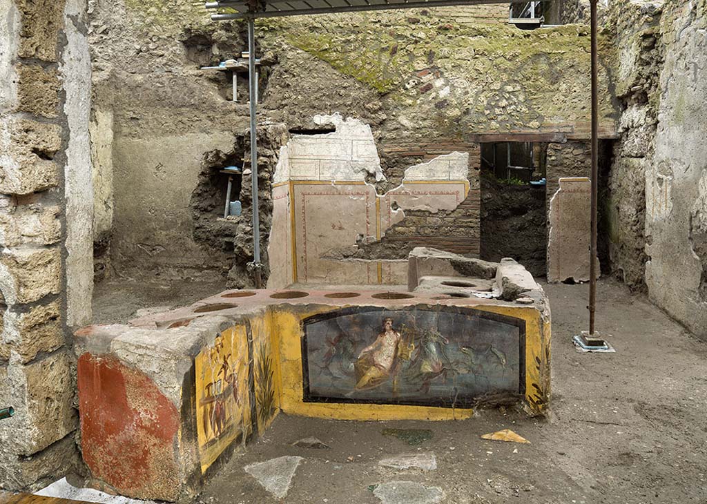 V.3 Pompeii, Thermopolium with painting of nereid. December 2020. Looking across the counter and rooms from the front entrance on the square in front of Vicolo delle Nozze d'Argento.
The flooring of the entire room consisted of a layer of cocciopesto (a waterproof covering made of terracotta fragments), into which fragments of polychrome marble (alabaster, portasanta, green breccia and bardiglio) were inserted in several areas.

V.3 Pompei, Termopolio con dipinto di nereide e anfore. Dicembre 2020. Guardando dall'altra parte del bancone e le camere dall'ingresso anteriore sulla piazza di fronte a Vicolo delle Nozze d'Argento.
Il piano pavimentale di tutto l'ambiente è costituito da uno strato di cocciopesto (rivestimento impermeabile composto da frammenti in terracotta), in cui in alcuni punti sono stati inseriti frammenti di marmi policromi (alabastro, portasanta, breccia verde e bardiglio).

Photo by Luigi Spina courtesy of Parco Archeologico di Pompei.
