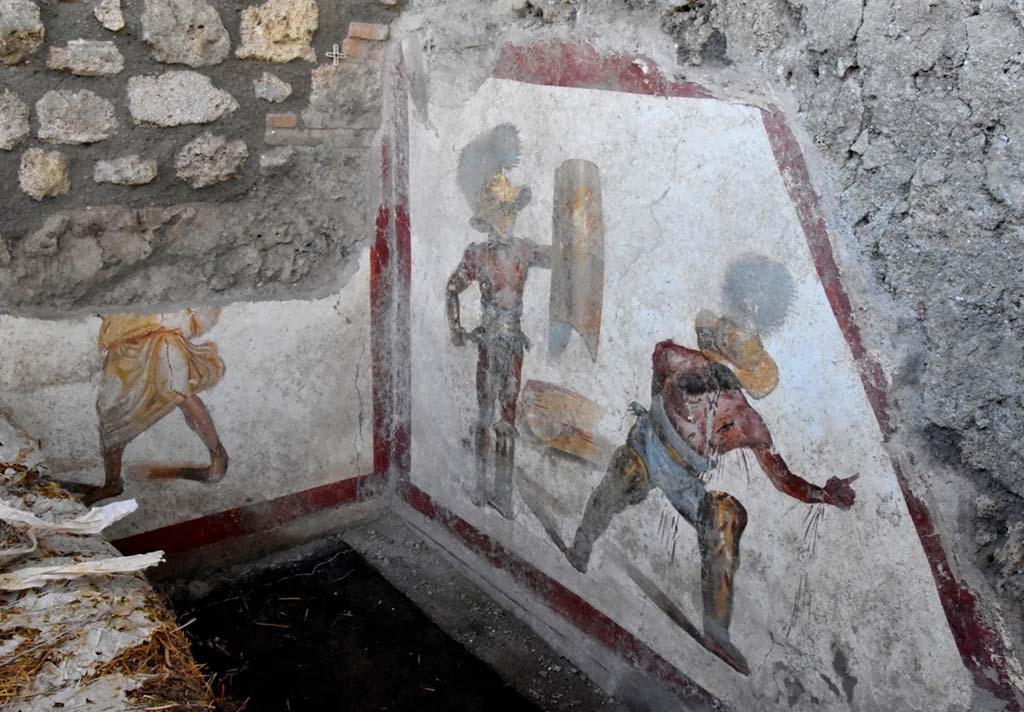 The fresco of about 1.12m x 1.5m, found in an environment behind the wide intersection of the Vicolo dei Balconi and the Vicolo delle Nozze d’Argento, has the shape of a trapezoid, as it was placed under the stairs, perhaps of a workshop. Above the painting, the imprint of the wooden staircase can be seen above the painting.  Most likely it decorated an environment frequented by gladiators, perhaps a bar equipped with an upper floor, intended for the accommodation of the owners of the business or as frequently, especially given the presence of gladiators, intended for prostitutes.

L’affresco di circa 1,12 mt x 1,5mt, rinvenuto in un ambiente alle spalle dello slargo di incrocio tra il Vicolo dei Balconi e il vicolo delle Nozze d’Argento, ha forma trapezoidale, in quanto era collocato nel sottoscala, forse di una bottega. Si intravede al di sopra della pittura, l’impronta della scala lignea.  Molto probabilmente decorava un ambiente frequentato da gladiatori, forse una bettola dotata di un piano superiore, destinato ad alloggio dei proprietari dell’esercizio commerciale o come di frequente, soprattutto vista la presenza di gladiatori, destinato alle prostitute.

Photograph © Parco Archeologico di Pompei.

Vedi http://pompeiisites.org/comunicati/laffresco-dei-gladiatori-combattenti-nuova-scoperta-nella-regio-v/
