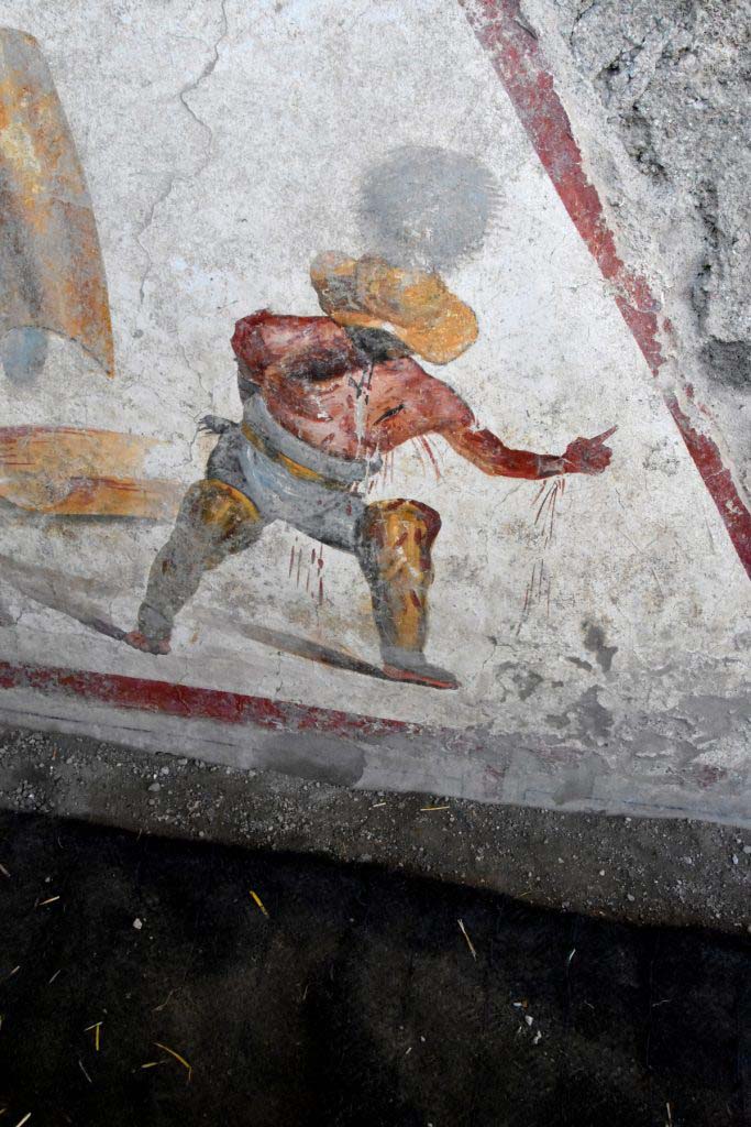 The other, in a succumbing position, is a "Thracian", a gladiator of the "Parmularii" category, with the shield on the ground. 
He is represented with a helmet (galea), with wide brim and wide visor to protect the face, topped by a tall crest.

L’altro, in posizione soccombente, è un “Trace”, gladiatore della categoria dei "Parmularii”, con lo scudo a terra. È rappresentato con elmo (galea), a tesa larga ed ampia visiera a protezione del volto, sormontato da un alto cimiero.

Photograph © Parco Archeologico di Pompei.
