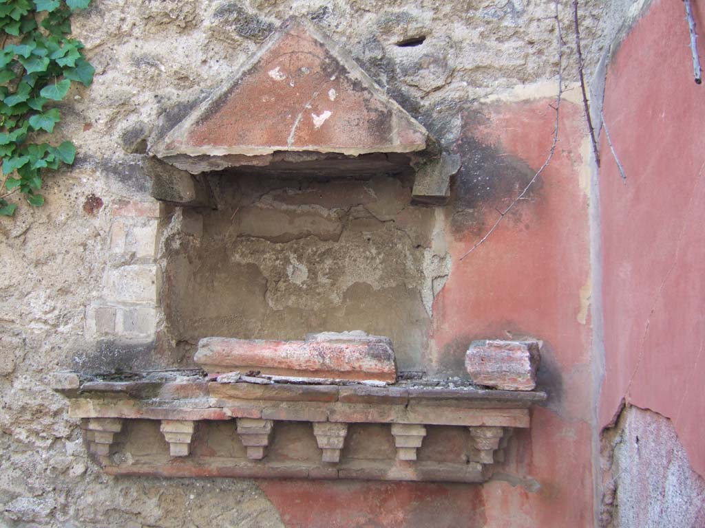 VI.15.23 Pompeii. September 2005. Lararium. 
According to Boyce, the three rooms in the south-west portion, to the right of the entrance, have bare walls without any decoration.
The kitchen in the corner is the exception, with the lararium on the west wall, in the north-west corner.
In the kitchen, the hearth is built against the west wall and between it and the north wall is the lararium.
A heavy ledge, held by consoles projecting from the wall, supported a temple façade constructed before a semicircular niche with flat ceiling.
The façade consisted of two Doric columns with bases and capitals, an architrave and a pediment.
The ledge and the aedicula were constructed of a mixture of brick and tufa.
The whole was painted red except for a star on a white ground in the centre of the tympanum.
See Boyce G. K., 1937. Corpus of the Lararia of Pompeii. Rome: MAAR 14.  (p.56, no.219, and Pl.15, 1 and 2)
See Fröhlich, T., 1991. Lararien und Fassadenbilder in den Vesuvstädten. Mainz: von Zabern. (L73 and Pict. 35,3) 
See Giacobello, F., 2008. Larari Pompeiani: Iconografia e culto dei Lari in ambito domestico. Milano: LED Edizioni. (p.183)
