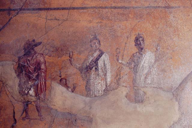 VI.16.7 Pompeii.  May 2006.  Room F, Peristyle.Lararium.  Painting of gods.  
Isis is in the centre wearing a red and black sash and holding a sistrum.  
Anubis is dressed in red.   A small figure between Isis and Anubis is possibly Harpocrates.  Serapis or Osiris is dressed in white with the horn of plenty in his left hand and a sistrum in his right.  See Fröhlich, T., 1991. Lararien und Fassadenbilder in den Vesuvstädten. Mainz: von Zabern. (L74, T. 38,1-2).
