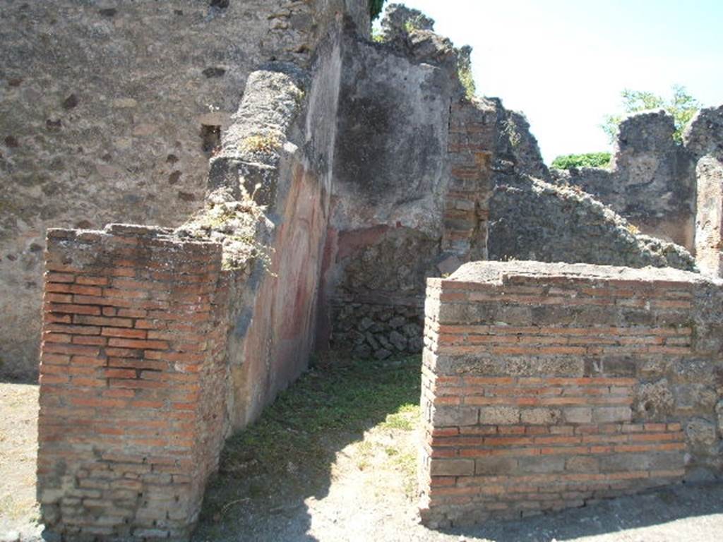 VI.16.20 Pompeii. May 2005. Looking west to entrance doorway. According to NdS, this rather narrow doorway led into a room that had a doorway in its north-west corner that communicated with the other rooms in VI.16.21/22/23/24. According to Sogliano, at one time the doorway to number 20 would have had a wooden threshold and perhaps also wooden doorjambs. The floor was of cocciopesto, and the wall dado was covered with red plaster. The walls were divided into the usual panels and pilasters on a yellow background.
The upper part was painted with white plaster. In the central panel on the south wall, on a red background one could see a painting of a deer being chased by a dog, enclosed in a rectangular cornice. On the opposite wall, one could still observe the lower part of a black cornice belonging to a painting that had been destroyed. The doorway into the adjoining rooms also would have had wooden doorjambs. See Notizie degli Scavi, 1908, (p.182)