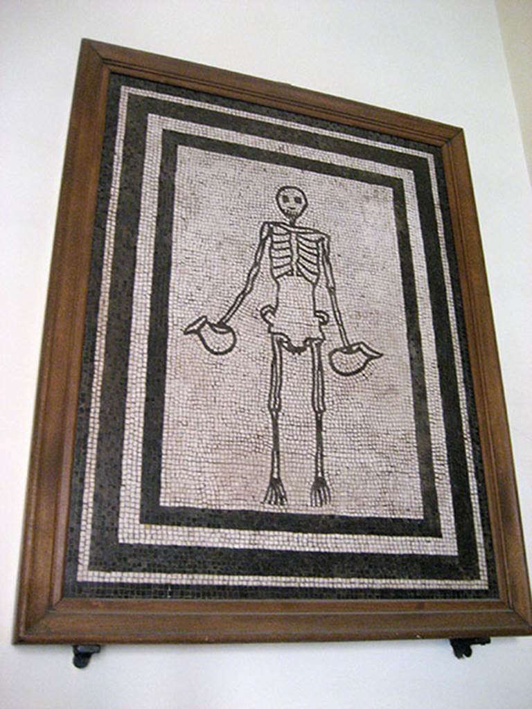 VI.17.19-26 Pompeii. Found in the week to 17th May 1783 in a room of a lower apartment. Mosaic of skeleton holding a jug in each hand.
Now in Naples Archaeological Museum. Inventory number 9978.
The parts of the walls that remained were painted black. In the middle was a red panel in which were painted some figures.
The room had a window with a threshold of ordinary white mosaic and here rested clearly a skeleton that held in each hand a jug made with black mosaic.
The floor of this room was of ordinary white mosaic with some black bands around it and many items of bronze, terracotta, glass, bone were found here.
See Pagano, M. and Prisciandaro, R., 2006. Studio sulle provenienze degli oggetti rinvenuti negli scavi borbonici del regno di Napoli. Naples: Nicola Longobardi, p. 80.